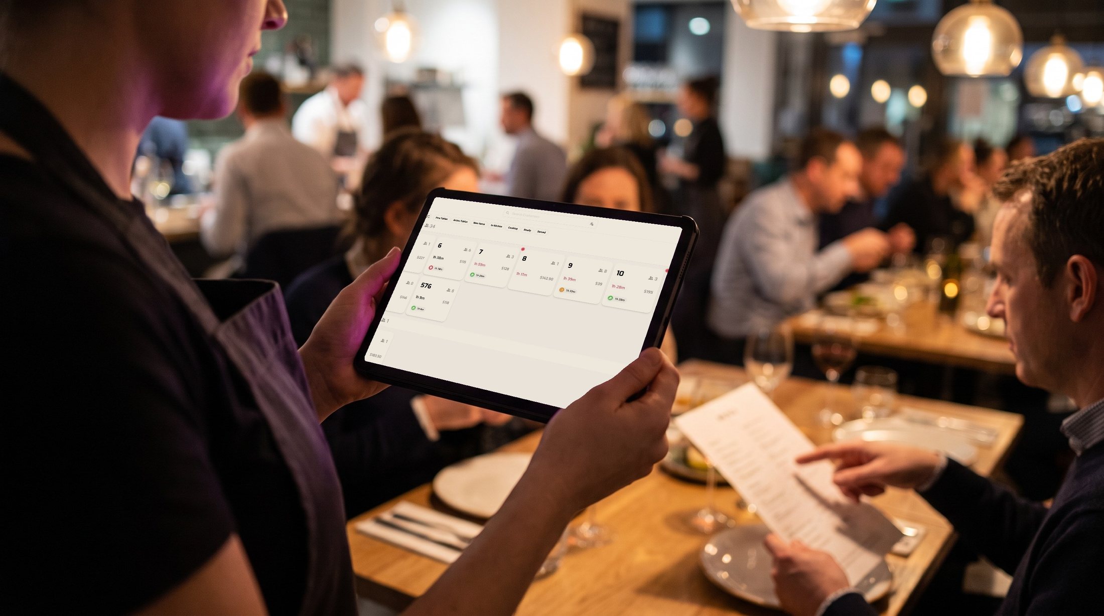 A waiter taking an order on an Asky tablet in a full dining room